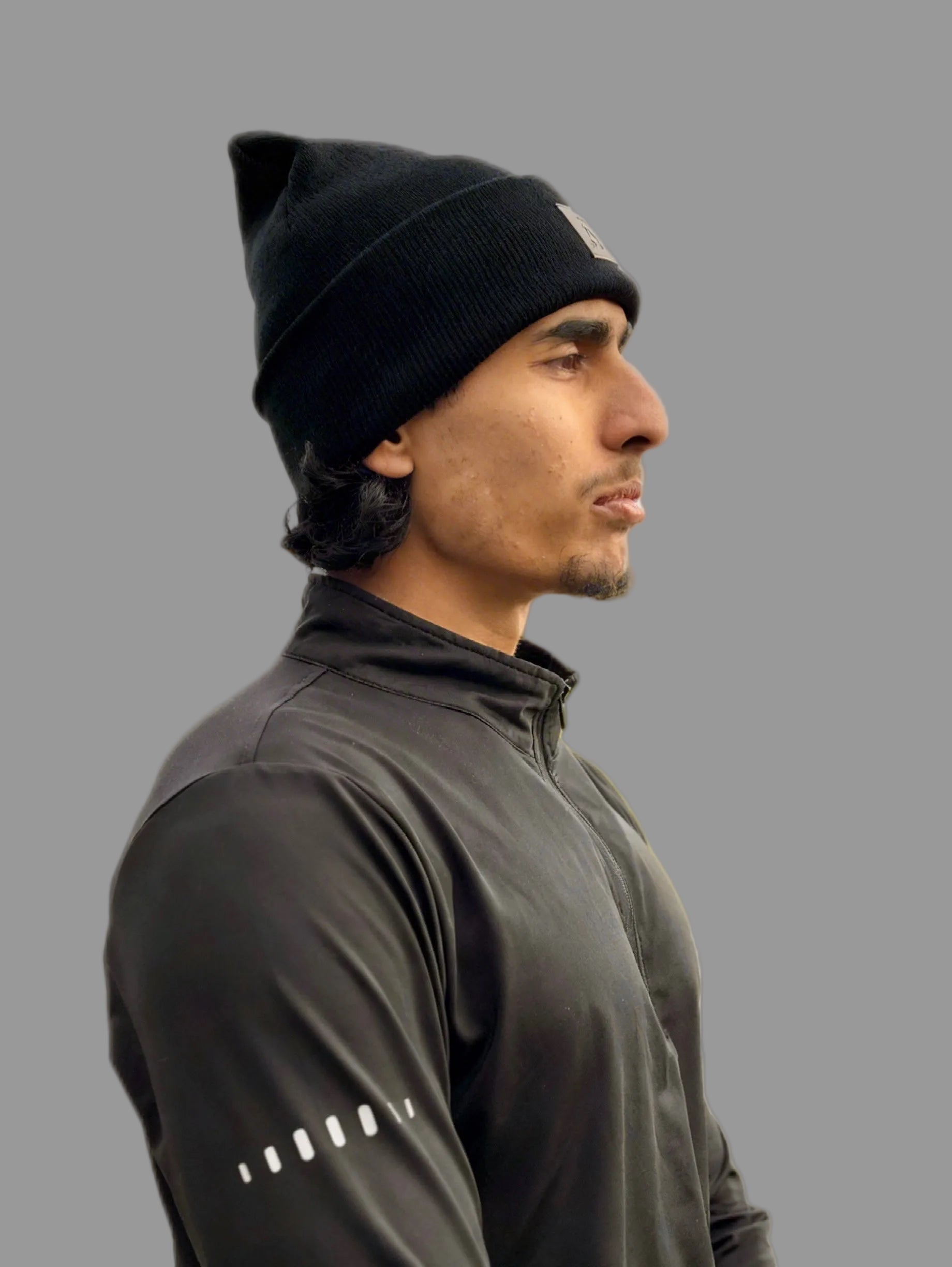 Man wearing a black beanie and quarter zip gym long sleeve top on a gray background