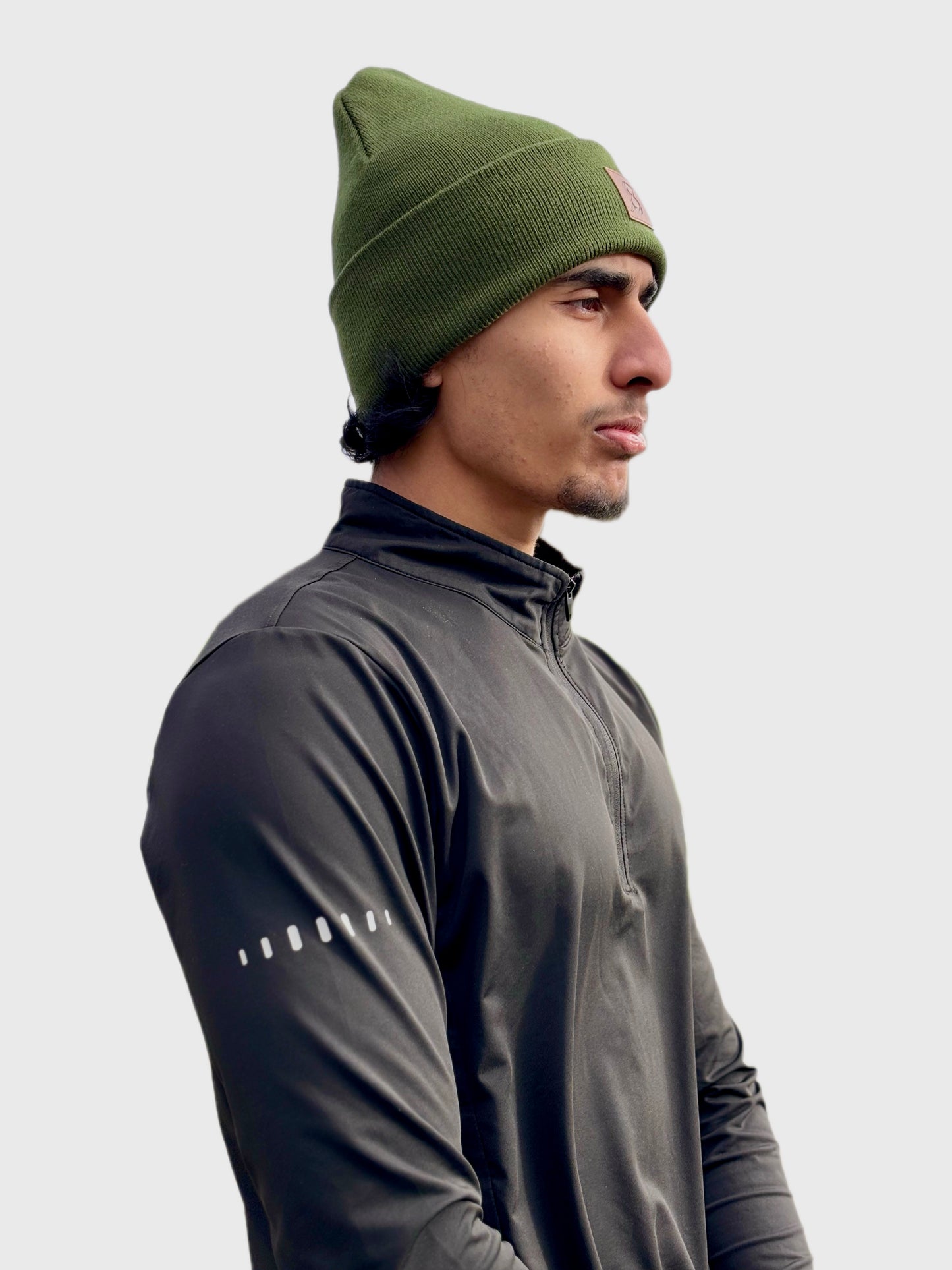 Man wearing a green beanie and dark jacket on a light gray background