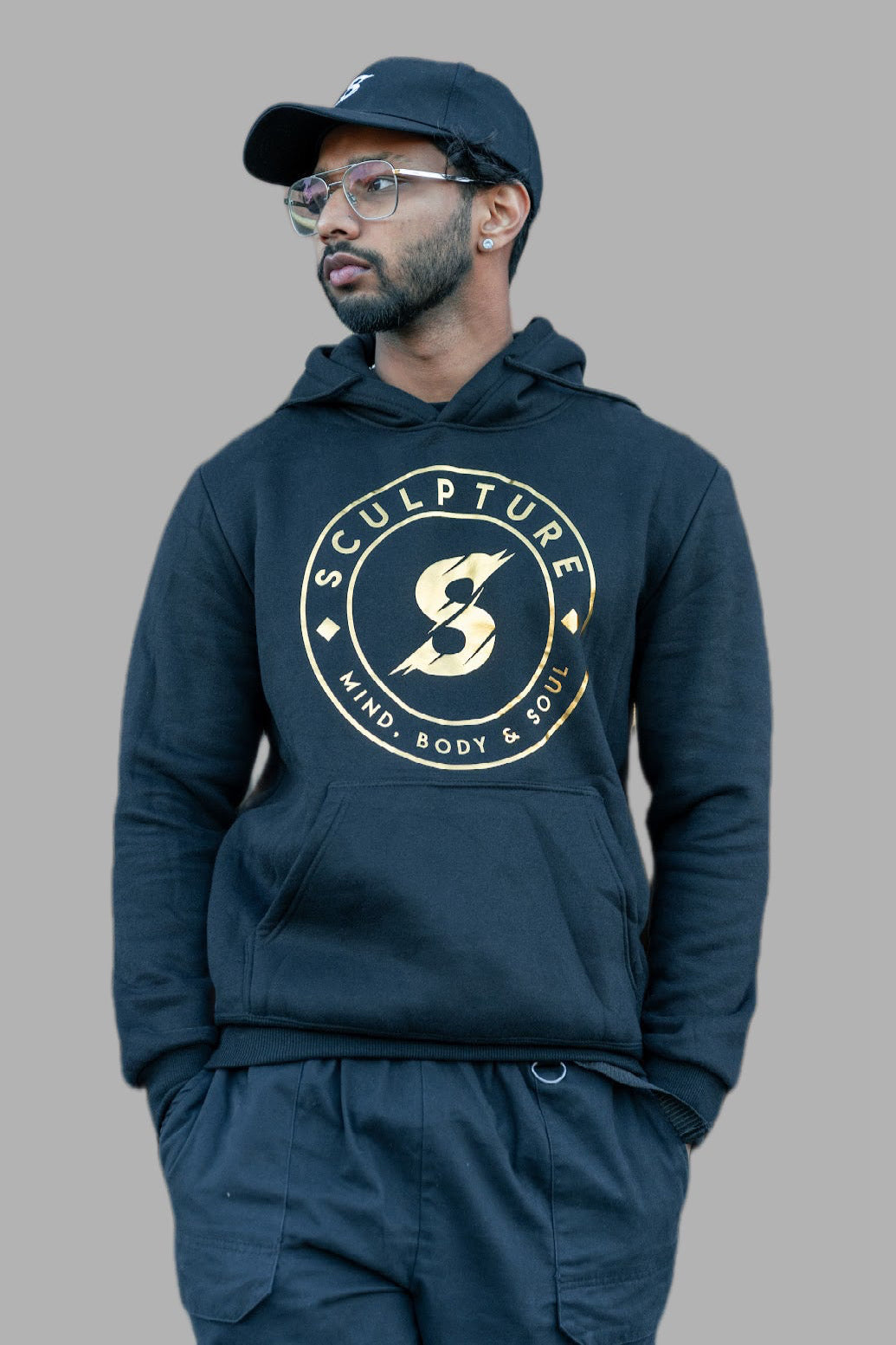 Man wearing a black hoodie with 'SCULPTURE' gold logo on a gray background